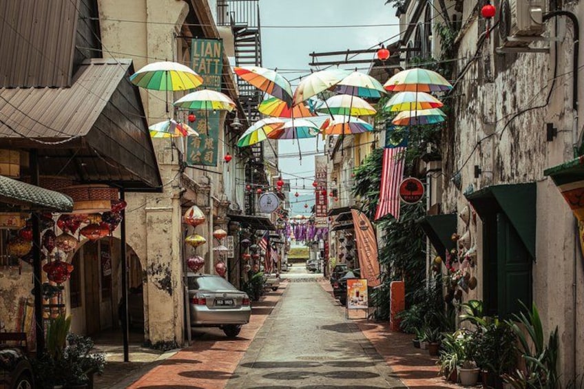 A narrow street with colorful umbrellas, traditional shops, and a car parked on the side. 2