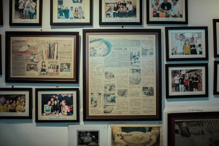 A wall with multiple framed photographs and a large framed newspaper. 5