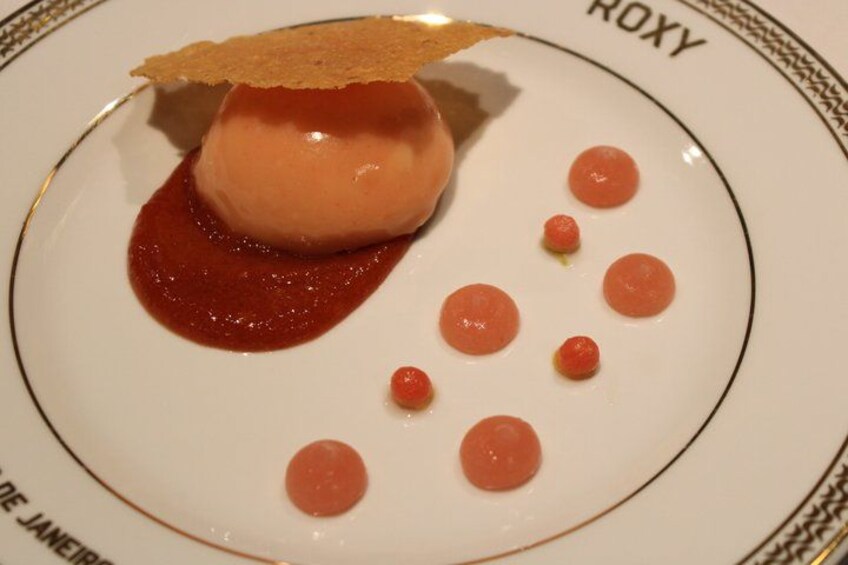 A dessert on a plate with a caramelized top, surrounded by small red spheres and a red sauce. 5