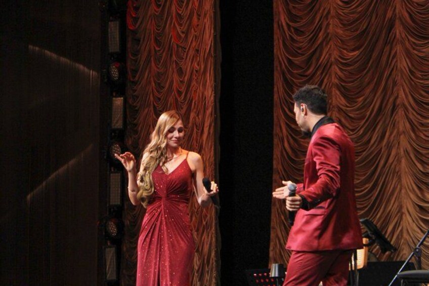 A person in a red suit and a person in a red dress on a stage with curtains. 3