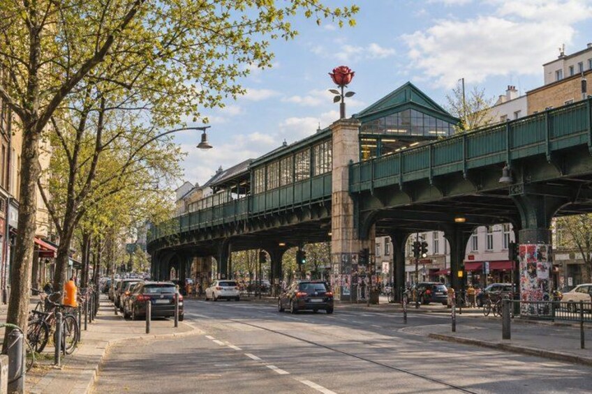 A street with a green pedestrian bridge, parked cars, and trees with green leaves. 5