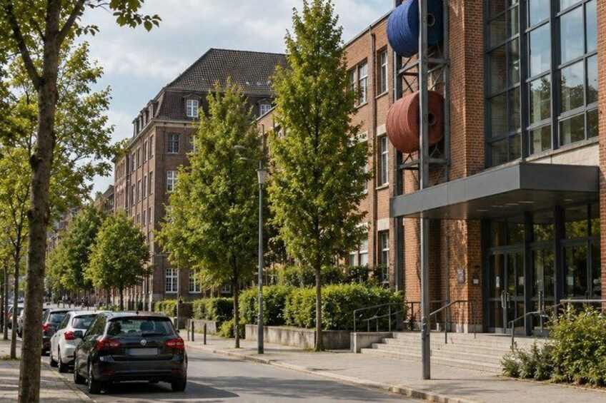 A street lined with parked cars, trees, and a modern building with large windows and a red brick facade. 3