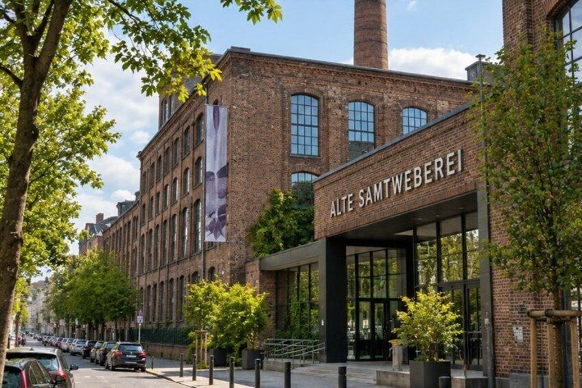 A brick building with a sign reading 'ALTE SAMTWEBEREI' and a modern glass entrance. 5