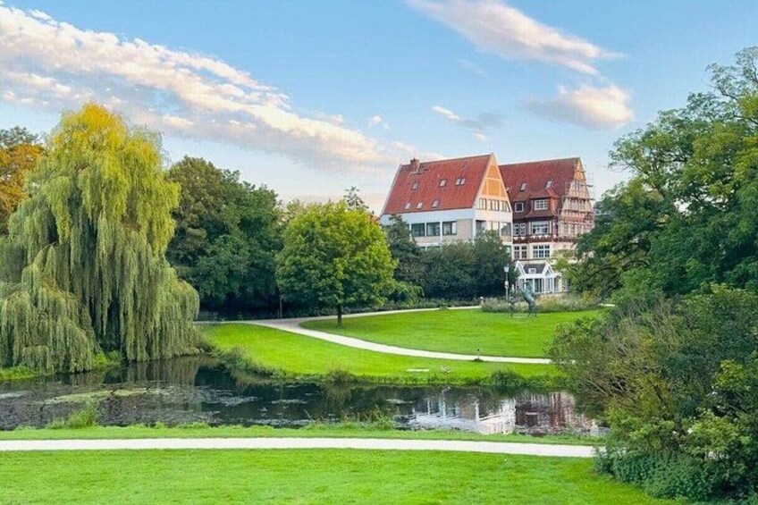 A park with a pond, trees, a pathway, and traditional houses. 4