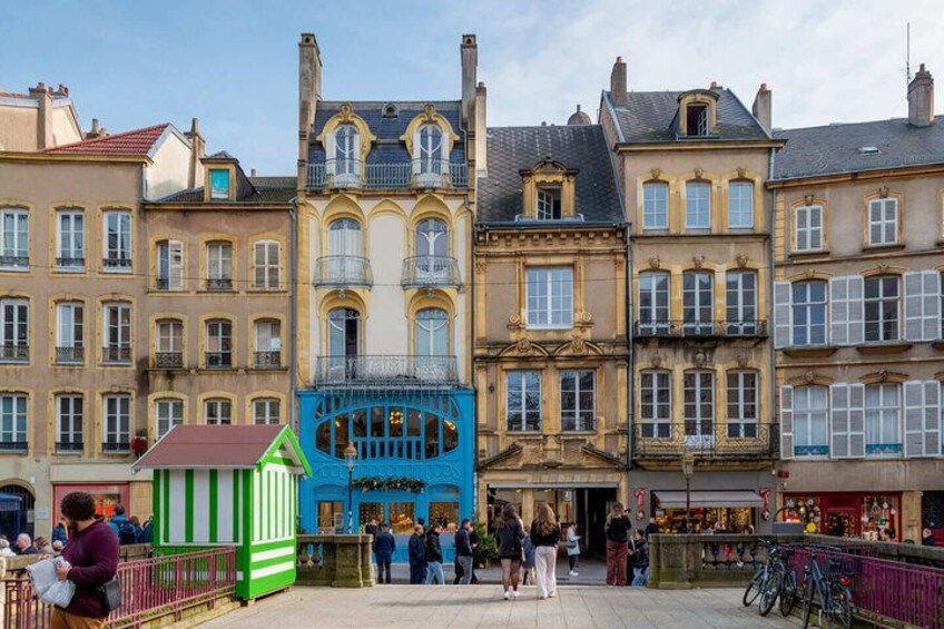 A historic European street with ornate buildings, a green and white striped structure, and people walking. 4