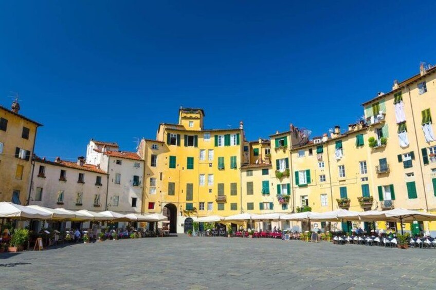 A square with buildings, outdoor seating, and a clear blue sky. 2