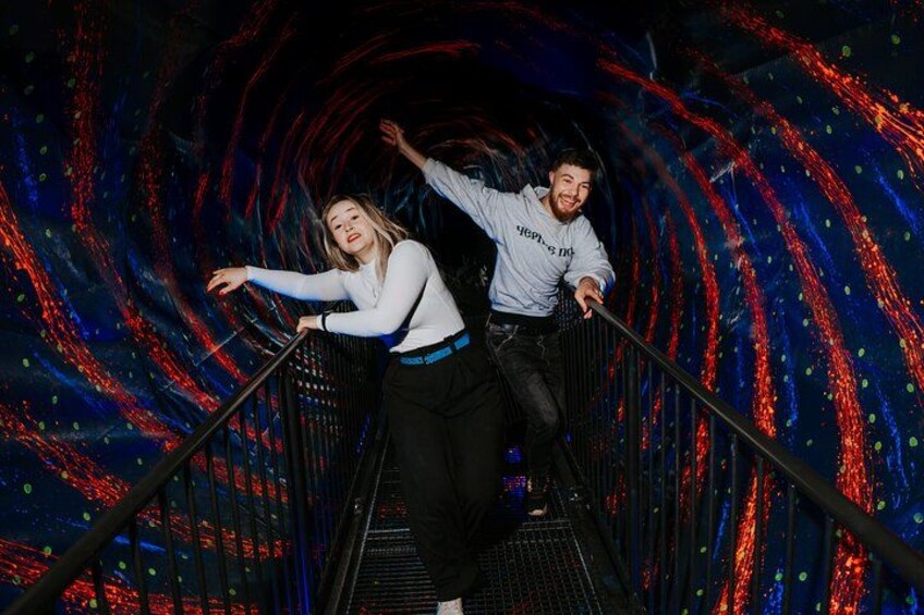 Two people on a moving walkway with a colorful, abstract background. 2