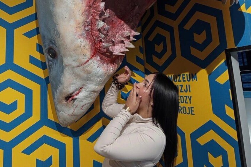 A person in front of a large fish sculpture with a geometric patterned background. 5