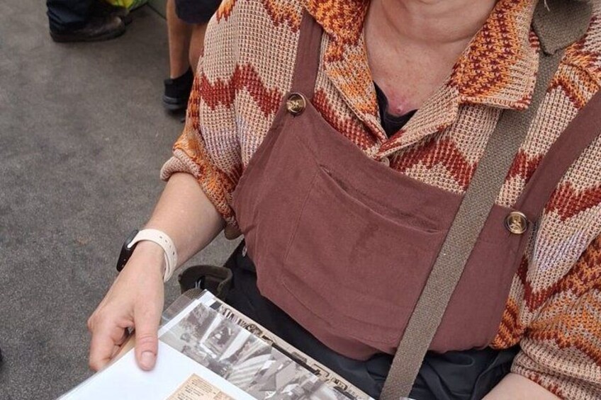 A person wearing a patterned shirt and a brown apron, holding a booklet. 2