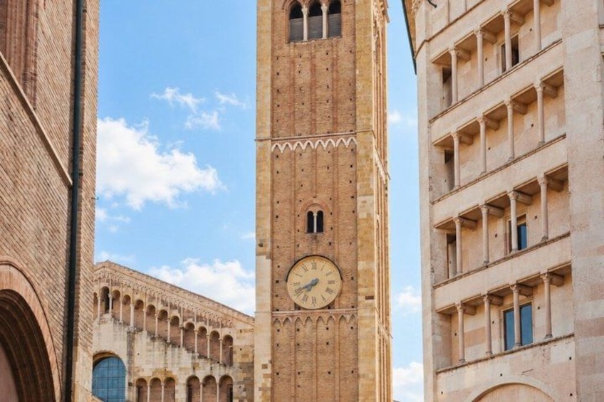 A tall clock tower with a circular face, surrounded by historic buildings with arched windows and detailed brickwork. 4
