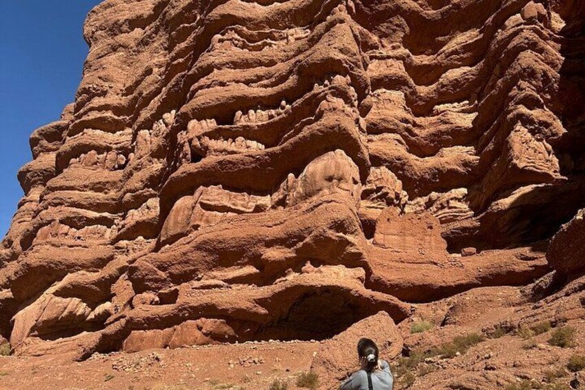 A large red rock formation with layered textures and a person standing in the foreground. 2