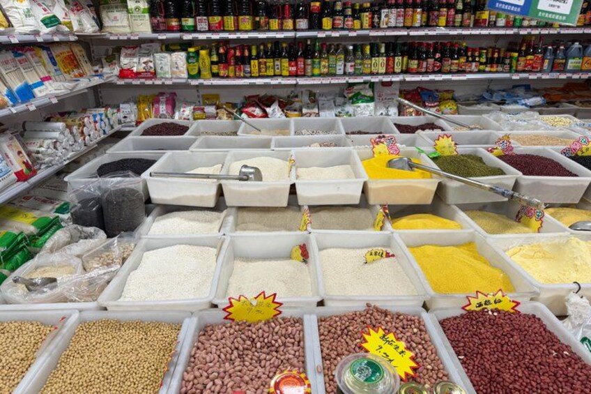 A variety of grains and legumes in bulk bins, with labels and price tags visible. 2