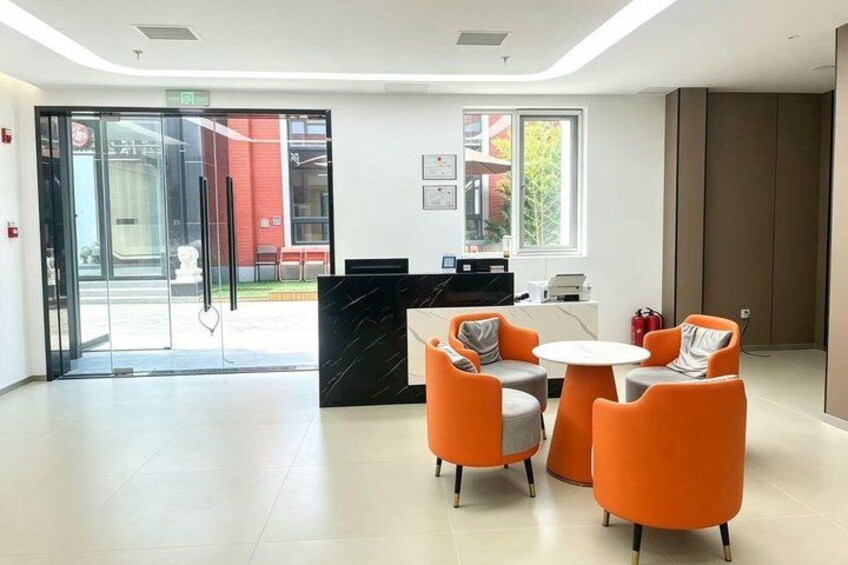 A modern reception area with a glass door entrance, a reception desk, and orange chairs around a small table. 4