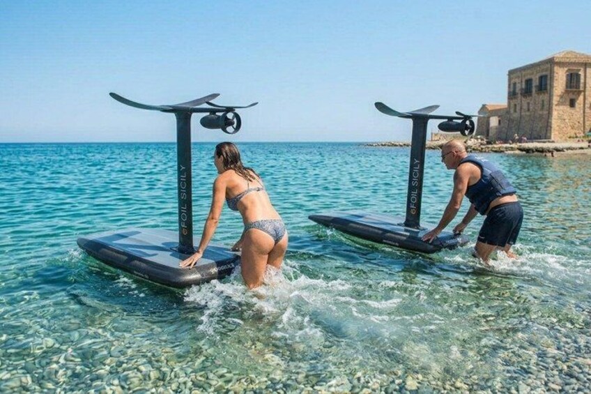 Two people using stand-up paddleboards on a clear body of water with a building in the background. 2