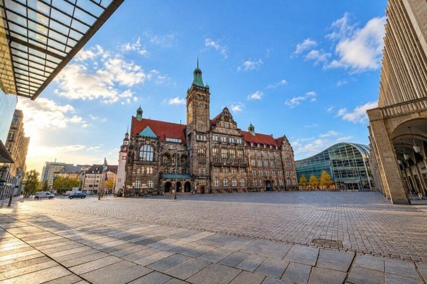 A historic building with a tower, a paved square, and modern architecture in the background. 4