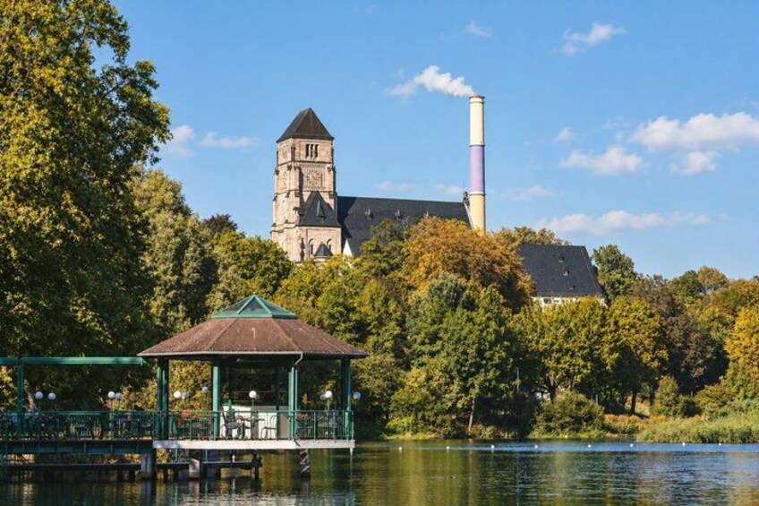 A historic church with a tower and a chimney, a gazebo by a lake, and trees in the background. 3