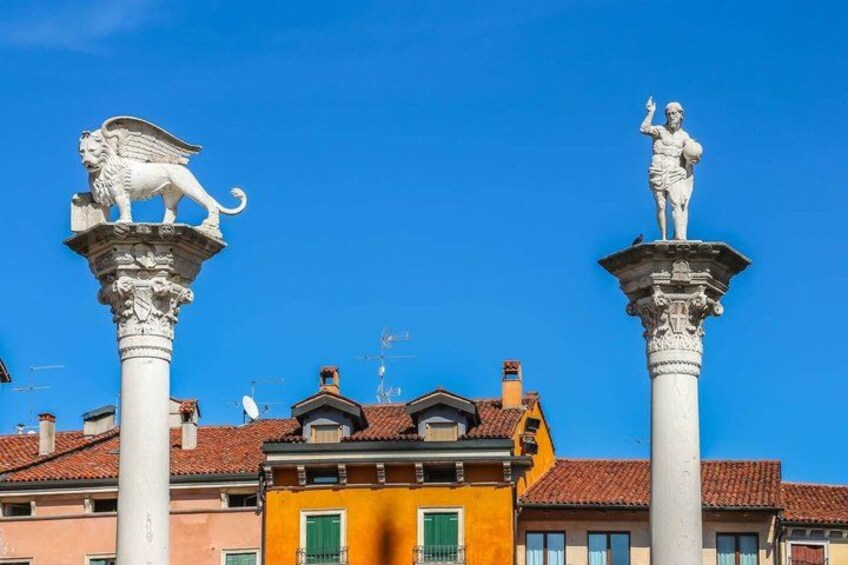 Two white statues on tall columns with buildings in the background. 3