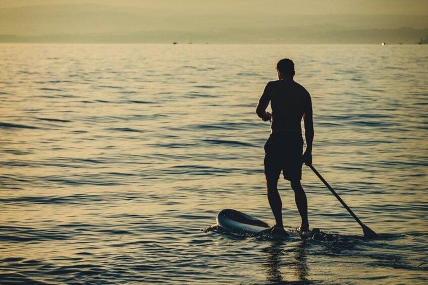 A person paddleboarding on calm water during sunset. 3