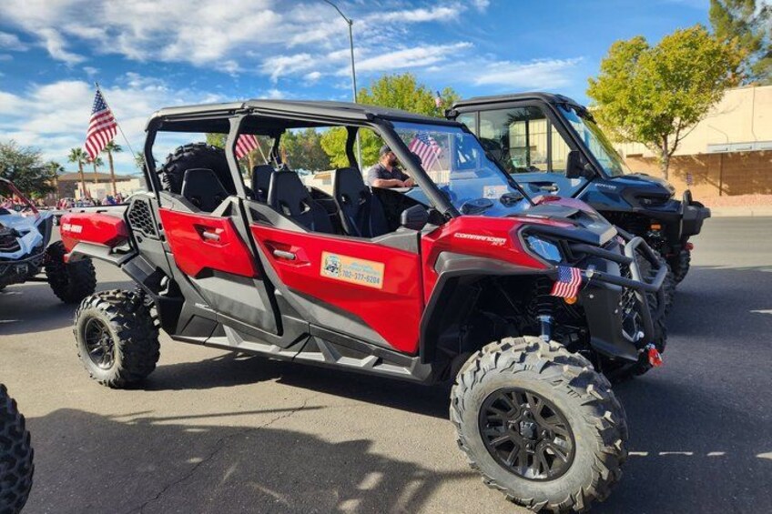 A red off-road vehicle with American flags on the front and side, parked on a road with other vehicles. 1