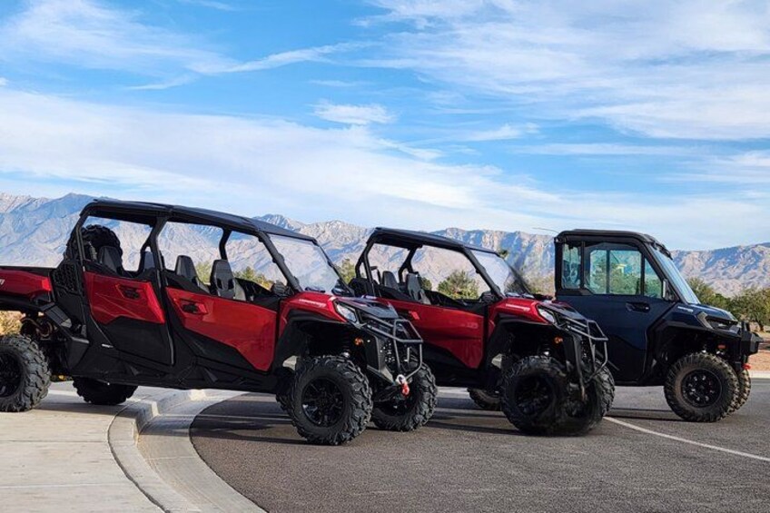 Three off-road vehicles parked on a paved surface with a mountainous landscape in the background. 2