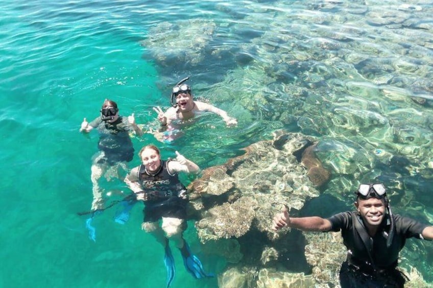 Four people snorkeling in clear blue water with visible underwater rocks. 1