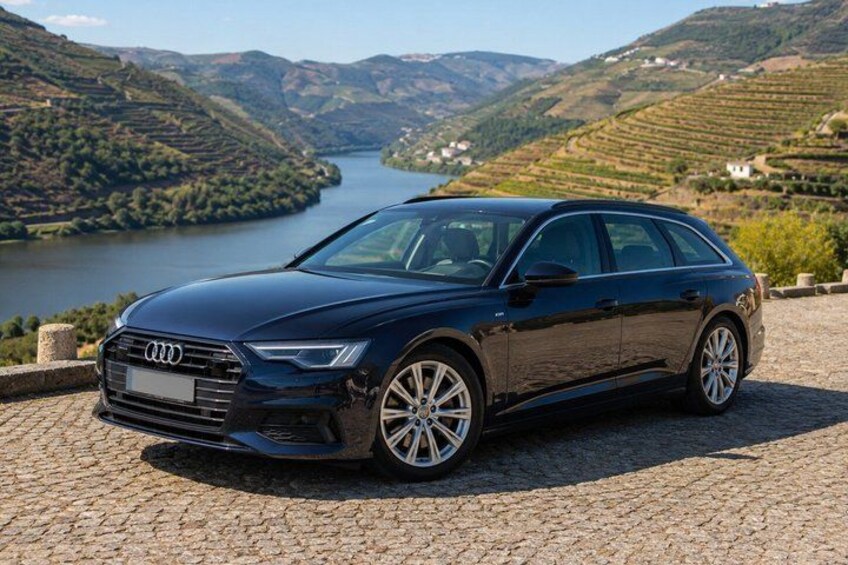 A black Audi car parked on a cobblestone path with a scenic view of a river and hills in the background. 5