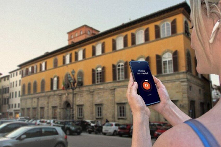 A person holding a smartphone with a map application open, standing in front of a historic building with arched windows and a red roof. 5