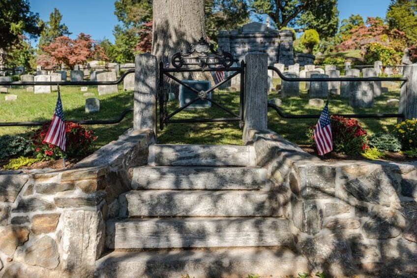 A cemetery with stone steps leading to a gate, American flags, and gravestones. 2