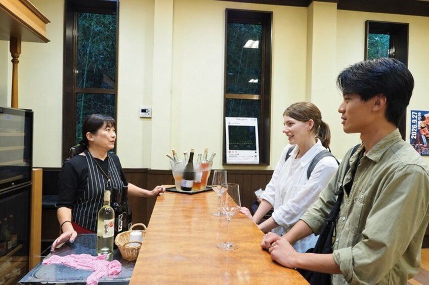 A group of people seated around a wooden table with wine glasses and bottles. 2