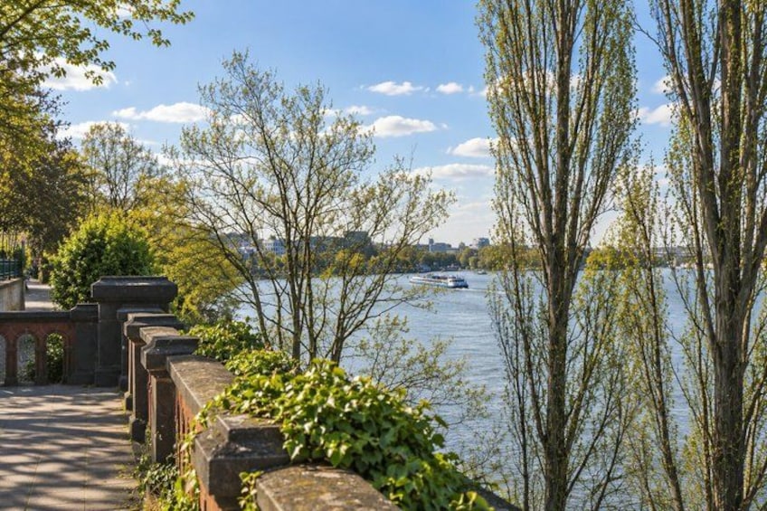 A riverside walkway with stone railings, trees, and a boat on the water. 2