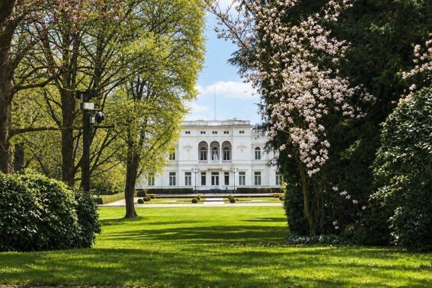 A large white building with arched windows, surrounded by well-manicured lawns and flowering trees. 5