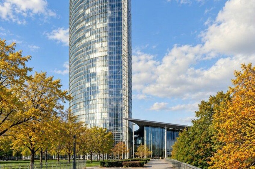 A tall glass skyscraper with a curved design, surrounded by trees with autumn foliage. 3