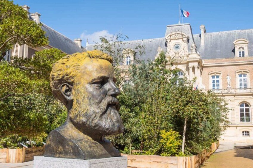 A bust sculpture in front of a historic building with a clock tower. 2