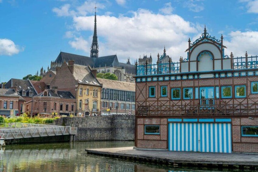 A historic town with a church spire, a colorful building with a blue and white striped awning, and a canal. 1