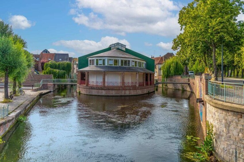 A canal with a houseboat, a stone bridge, and trees. 4