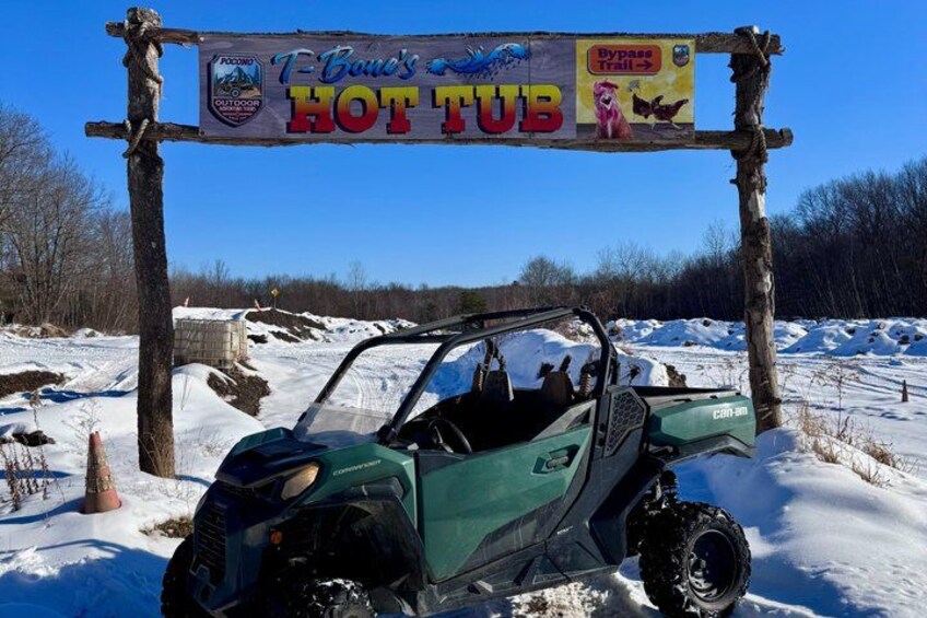 A green ATV parked in a snowy area with a sign above it that reads 'T-Bone's HOT TUB.' 4