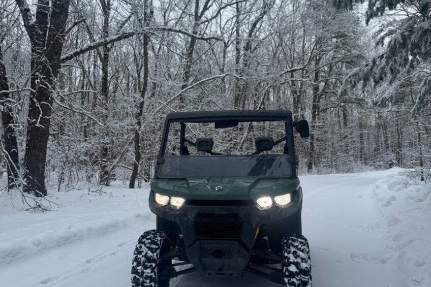 A green off-road vehicle on a snow-covered path in a forest. 3