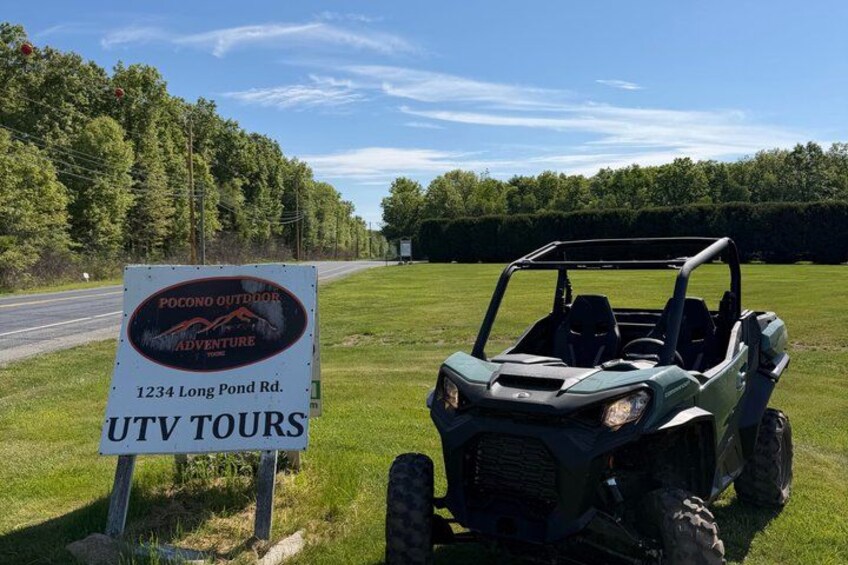 A sign for Pocono Outdoor Adventure at 1234 Long Pond Rd. and a green UTV. 1