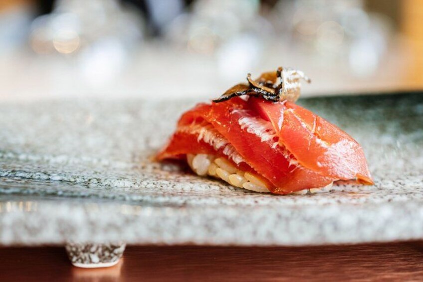 A piece of sushi with salmon on a textured surface. 5