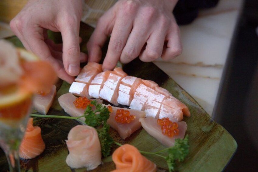 A person slicing sashimi on a wooden board with garnishes. 3