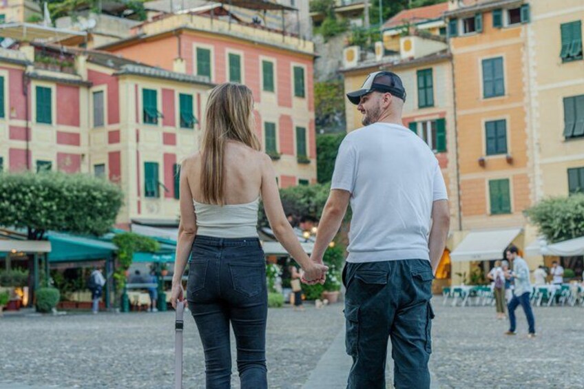 A couple holding hands in a cobblestone square with colorful buildings in the background. 5