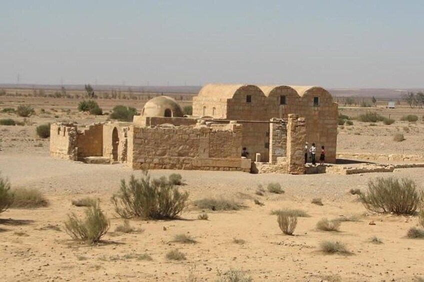 A desert landscape with a historical stone structure featuring domed roofs and arches. 1