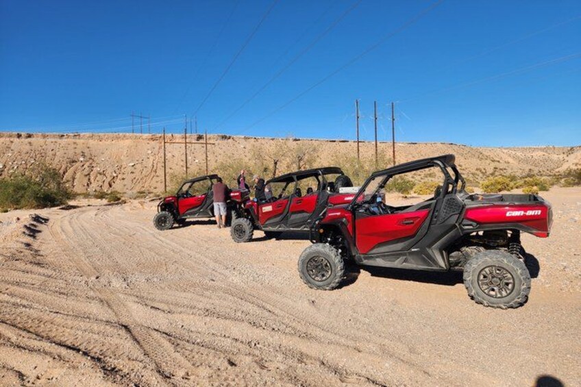 Three red off-road vehicles parked on a dirt road with a clear blue sky and a desert landscape in the background. 2