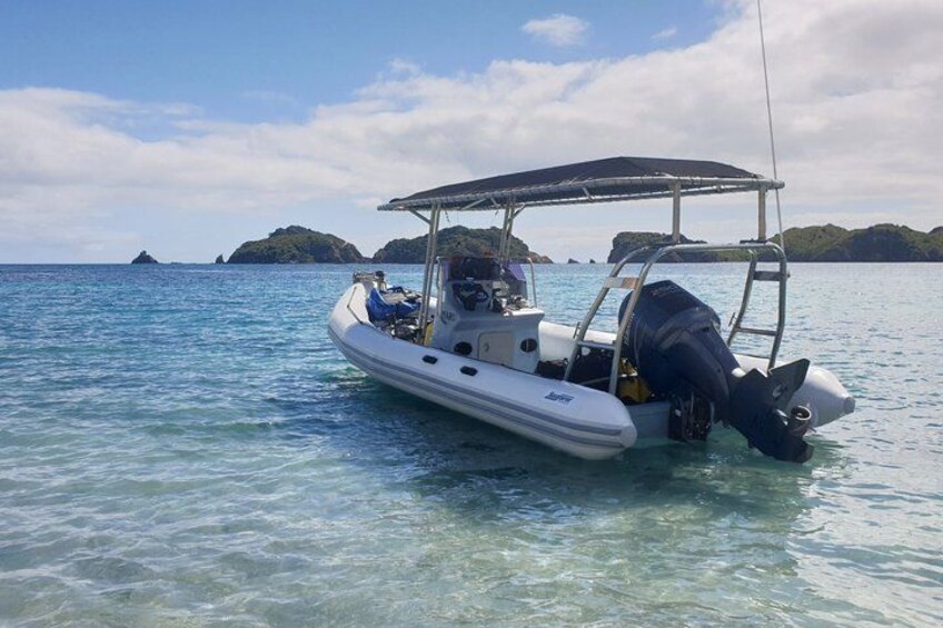 A small motorboat on calm water with a canopy, surrounded by clear water and distant islands. 5