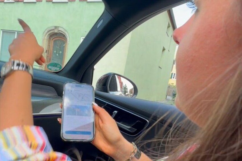 A person holding a smartphone inside a car, with a building visible through the window. 3