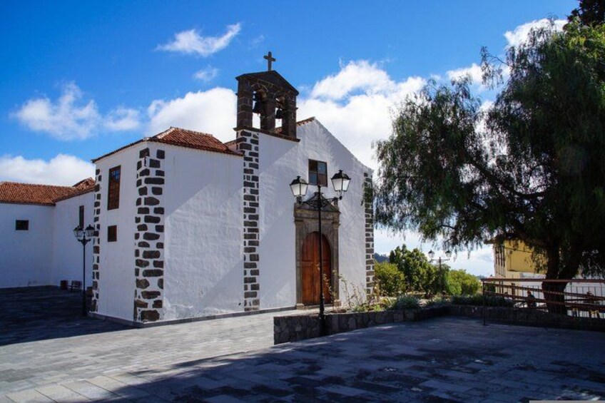A white church with a bell tower, a stone wall, and a paved courtyard. 2