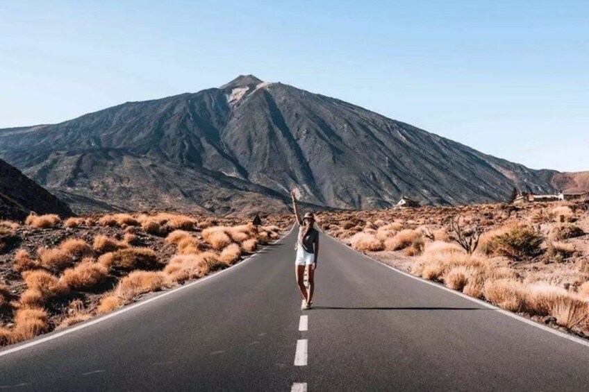 A road with a person standing on the side, a mountain in the background, and dry grass on the sides. 1