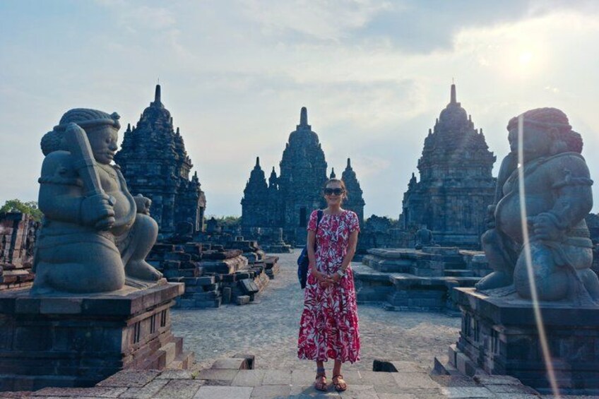 A person standing in front of ancient stone structures with intricate carvings, surrounded by similar stone figures and a large temple in the background. 5
