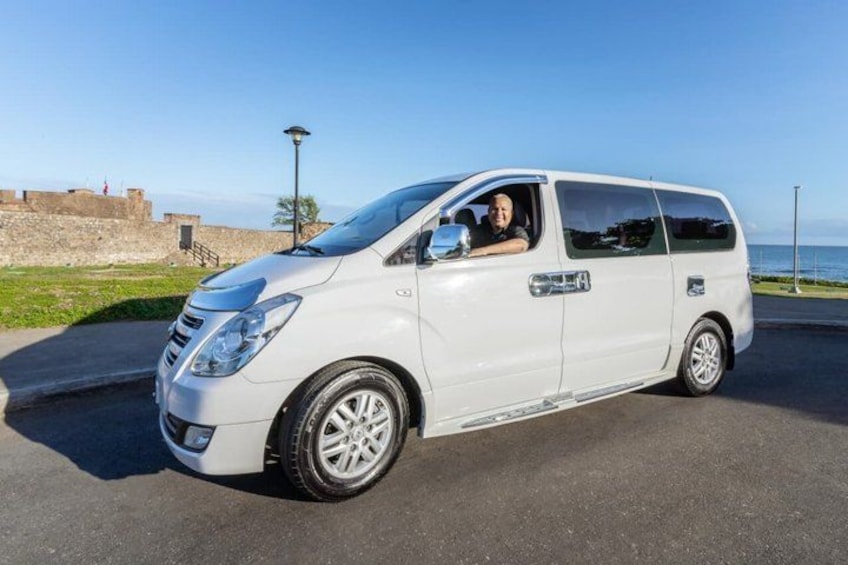 A white van parked on a paved area with a clear sky and a distant view of a body of water. 3