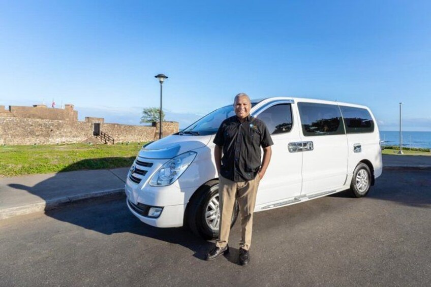 A white van parked on a paved area with a clear sky and a coastal landscape in the background. 2